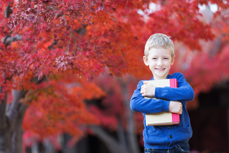 beautiful little schoolboy holding book ready for new school year in the autumn parkの写真素材