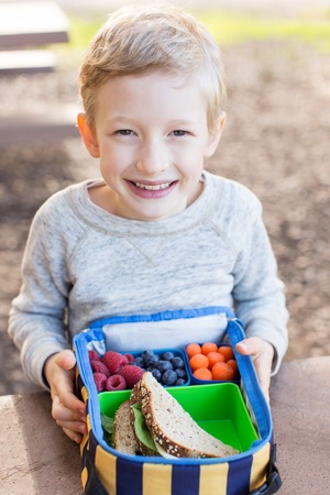 cheerful schoolboy eating healthy lunch outdoorの写真素材