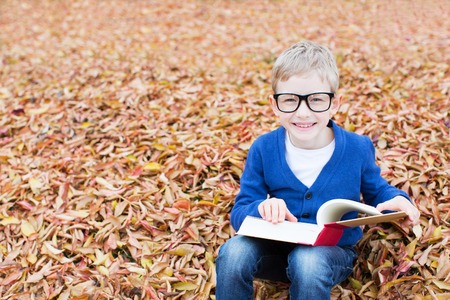 cheerful schoolboy in glasses holding book and ready for schoolの写真素材