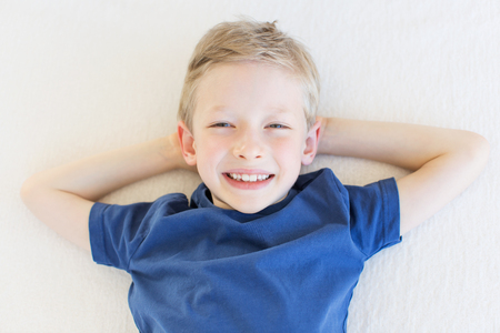 portrait from above of beautiful smiling boy expressing positive emotions lying down and relaxing during vacationの写真素材