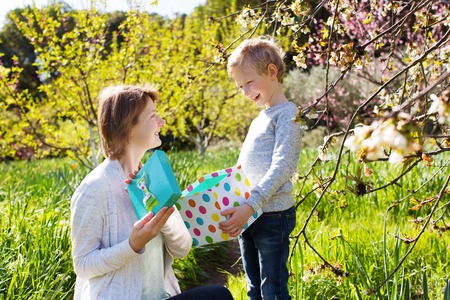 young beautiful mother and her adorable son sitting together in the park at spring time celebrating...