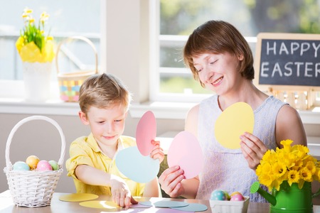 happy smiling family of two enjoying easter time at home, doing crafts, easter themed decorations and blackboard sign "happy easter!" in the backgroundの写真素材