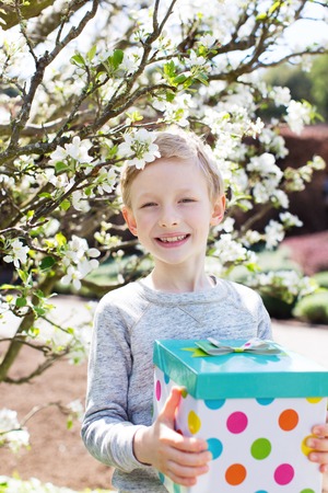 cheerful smiling boy holding colorful present for mother's day or other celebration by the blooming tree at park at spring timeの写真素材