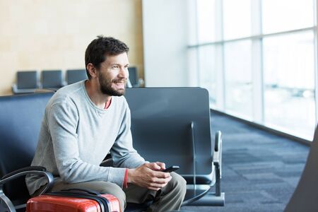 handsome smiling man with a beard holding mobile phone and working at the airport, technology, travel and modern life conceptの写真素材