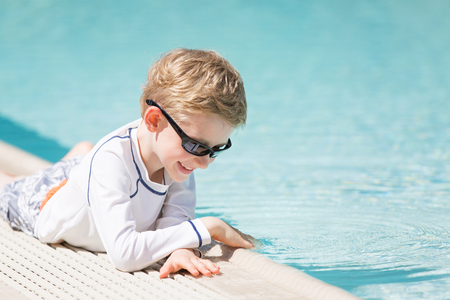 smiling excited boy in sunglasses and rashguard enjoying warm weather in swimming pool, vacation and sun protection conceptの写真素材