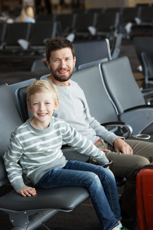 happy positive family of two, father with a beard and little son, at the airport waiting for departure, travel and vacation conceptの写真素材