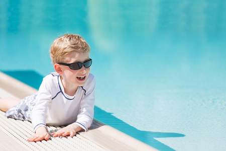 smiling excited boy in sunglasses and rashguard enjoying warm weather in swimming pool, vacation and sun protection conceptの写真素材