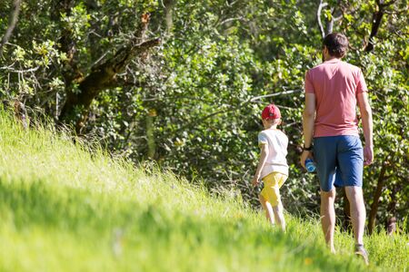 back view of father and his son walking or hiking in the parkの写真素材