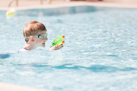 smiling excited boy with beach toy in goggles and rashguard enjoying warm weather in swimming pool, vacation and sun protection conceptの写真素材