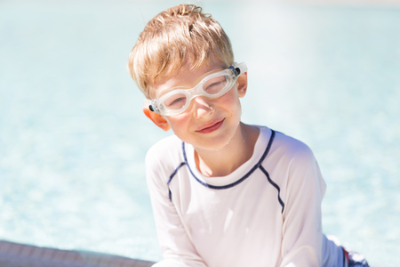 smiling excited boy in goggles and rashguard enjoying warm weather in swimming pool, vacation and sun protection conceptの写真素材