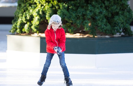 smiling positive boy enjoying ice skating at outdoor skating rink with christmas tree in the background, winter holiday or vacation activityの写真素材
