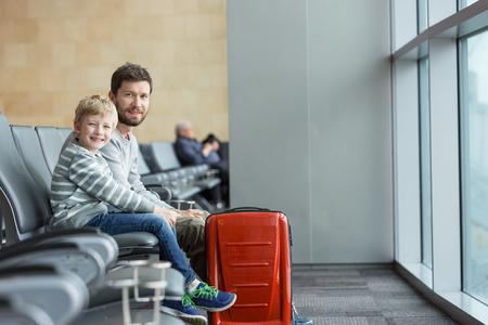 family of two smiling sitting and waiting for airplane departure at airport terminal, vacation and transportation conceptの写真素材