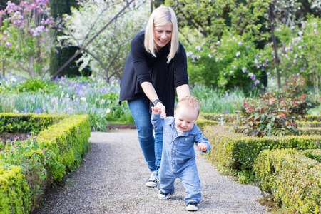 laughing cute toddler boy running away from young mother making first steps enjoying time together in the parkの写真素材
