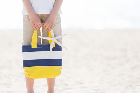 picture of boy holding colorful beach bag and starfish at the beach with no face visible with copyspace on the side, vacation conceptの写真素材