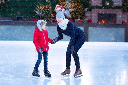 family of two enjoying ice skating at winter at outdoor skating rink decorated for holiday time at snowy weather, winter and family conceptの写真素材