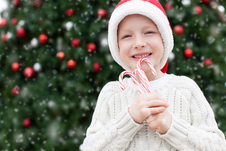 little boy in santa's hat holding candy canes enjoying snowy christmas timeの写真素材