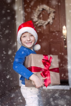 little boy in santa's hat holding christmas gift enjoying snowy christmas timeの写真素材