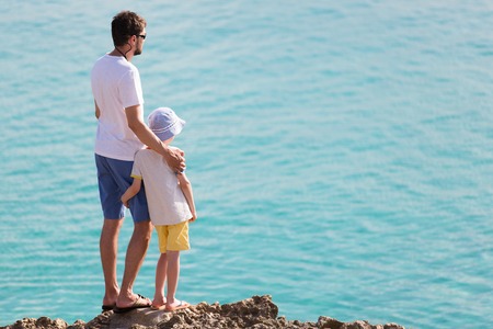 back view of family of two standing together at rocky beach enjoying sunset and summer vacation at anguilla islandの写真素材