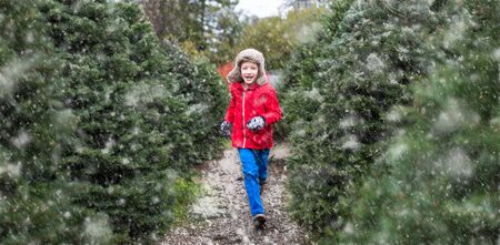 smiling cheerful boy in trapper hat and warm winter clothes running at christmas market enjoying the holiday season, snowy weatherの写真素材