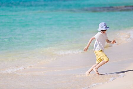 caucasian little boy running from waves at picture perfect beach enjoying summer vacation, copyspace on the leftの写真素材