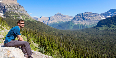 panorama of young man enjoying gorgeous mountain and valley view in glacier national park, montana state, usaの写真素材