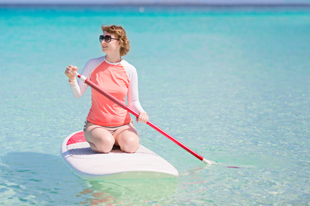 young woman in rashguard enjoying stand up paddleboarding at beautiful caribbean lagoon, active vacation conceptの写真素材