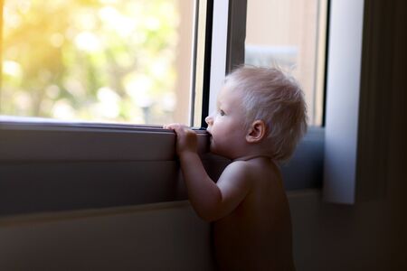 adorable blond toddler looking out of windowの写真素材