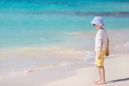 caucasian little boy standing at picture perfect beach enjoying summer vacation, copyspace on the leftの写真素材