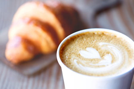close-up of beautiful heart shaped latte art with croissant pastry in the background in cafeの写真素材