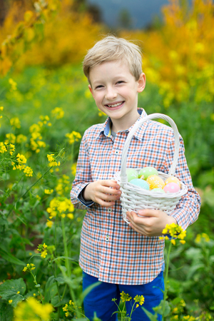 cheerful caucasian boy with basket full of easter eggs after egg hunt at beautiful field of blooming spring flowersの写真素材