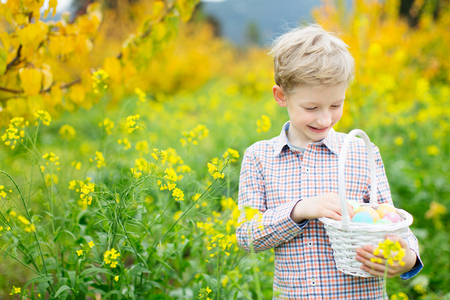 cheerful caucasian boy with basket full of easter eggs after egg hunt at beautiful field of blooming spring flowersの写真素材