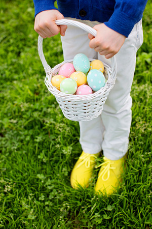 little boy holding white basket with easter eggs after egg hunt standing at grass in the parkの写真素材