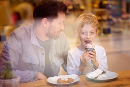 family of two, father and son, spending time together and enjoying desserts in cafeの写真素材