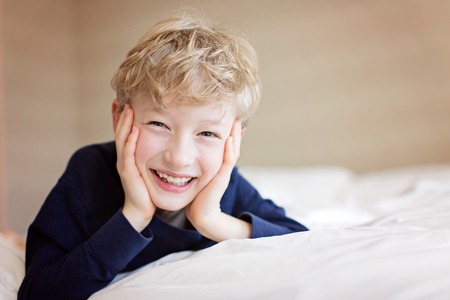 beautiful laughing boy lying in the bed being playful and happy, positive emotion conceptの写真素材