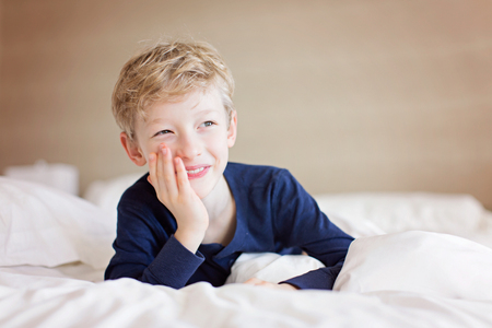 beautiful laughing boy lying in the bed being playful and happy, positive emotion conceptの写真素材