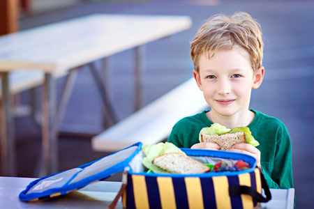 beautiful positive schoolboy enjoying healthy lunch during recess outdoorの写真素材