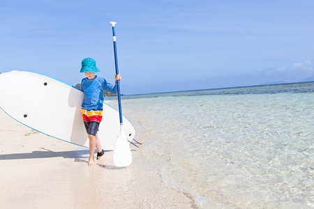 positive smiling boy enjoying stand up paddleboarding, active healthy vacation concept, wide angle with copy space on rightの写真素材