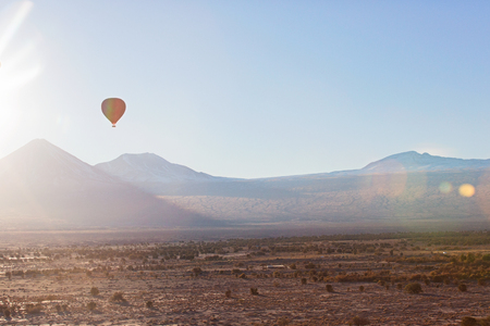 beautiful scenic landscape in atacama desert, chile with flying hot air balloon at sunrise with sun flareの写真素材