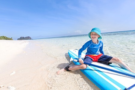 positive smiling boy enjoying stand up paddleboarding, active healthy vacation concept, wide angle with copy space on leftの写真素材
