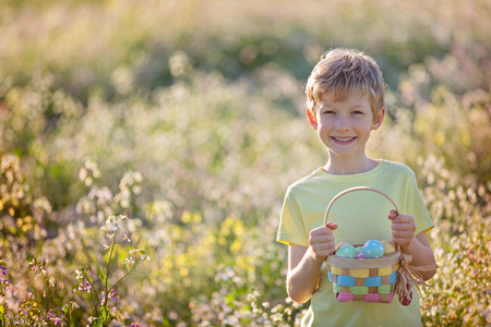 cheerful little boy holding basket full of easter eggs after egg hunt at beautiful blooming field at spring timeの写真素材