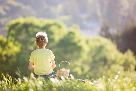cheerful little boy with basket full of easter eggs after egg hunt in beautiful park at spring timeの写真素材