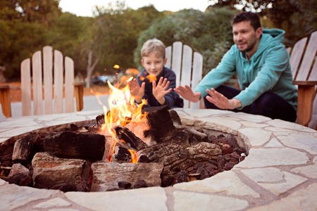 view of firepit and happy smiling family of two, father and son, warming their hands by the fire and enjoying time together in the backgroundの写真素材