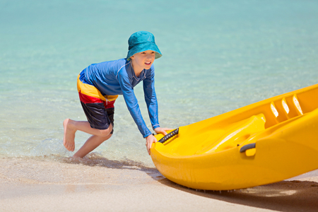 active little boy pushing kayak to the sand, enjoying vacation at tropical islandの写真素材