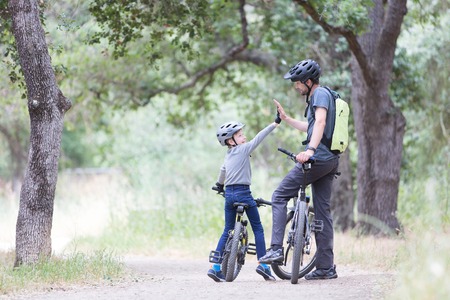 family of two, young father and cheerful son, enjoying bike riding, kid giving high five to his dad, active family conceptの写真素材