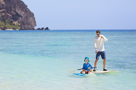 family of two, little boy and young father, enjoying stand up paddleboarding together at fiji, active family vacation conceptの写真素材