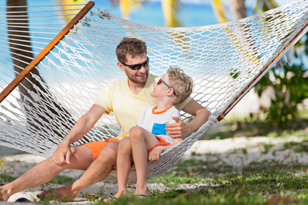 smiling family of two, father and son, enjoying summer tropical vacation together in hammock, father's day conceptの写真素材