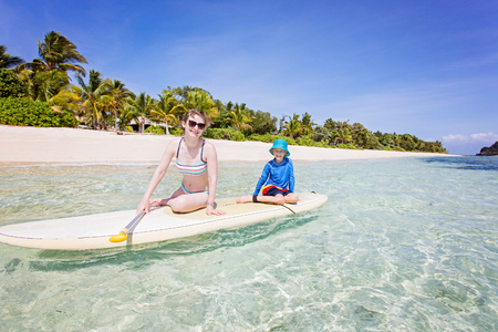 wide angle shot of family of two, mother and son, enjoying stand up paddleboarding in beautiful turquoise lagoon at fiji island, active vacation conceptの写真素材