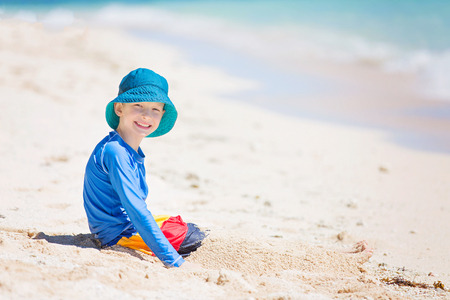 cheerful little boy in sunhat and rashguard playing in the sand at tropical beach, sun protection conceptの写真素材