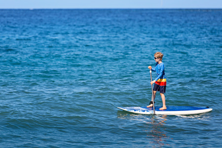 little boy stand up paddleboarding alone, enjoying active vacation at lanai island, hawaii, copy space on leftの写真素材