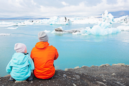 back view of family of two, father and son, enjoying the gorgeous view of icebergs in jokulsarlon lagoon in iceland, family active adventure vacation concept, copy space on rightの写真素材